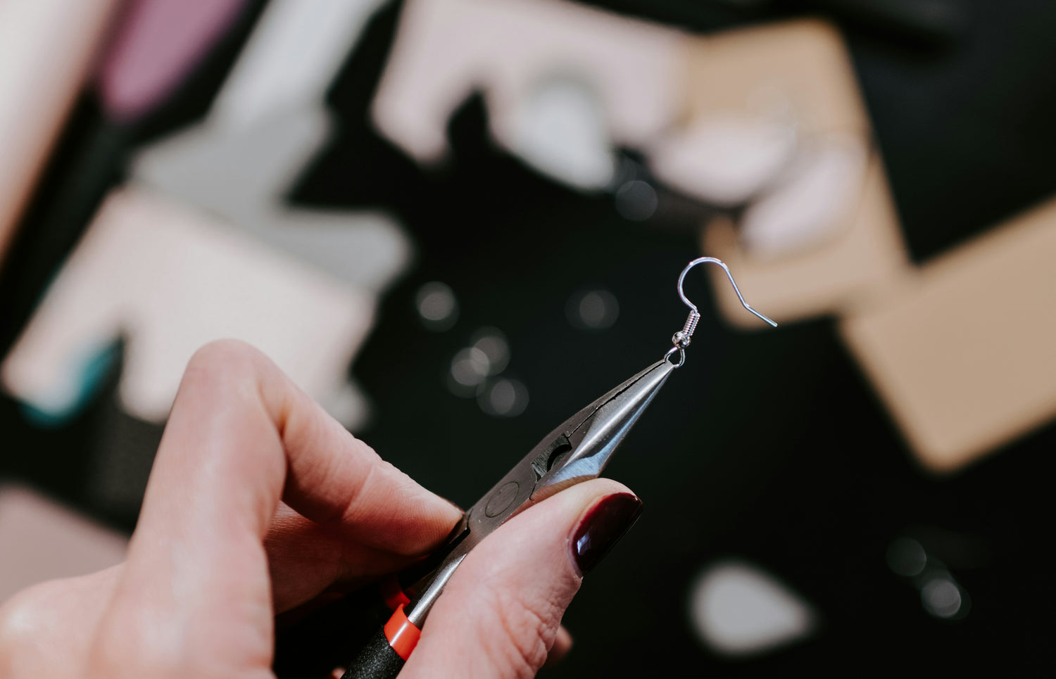 Hand holding plyers that are picking up an earring hook.
