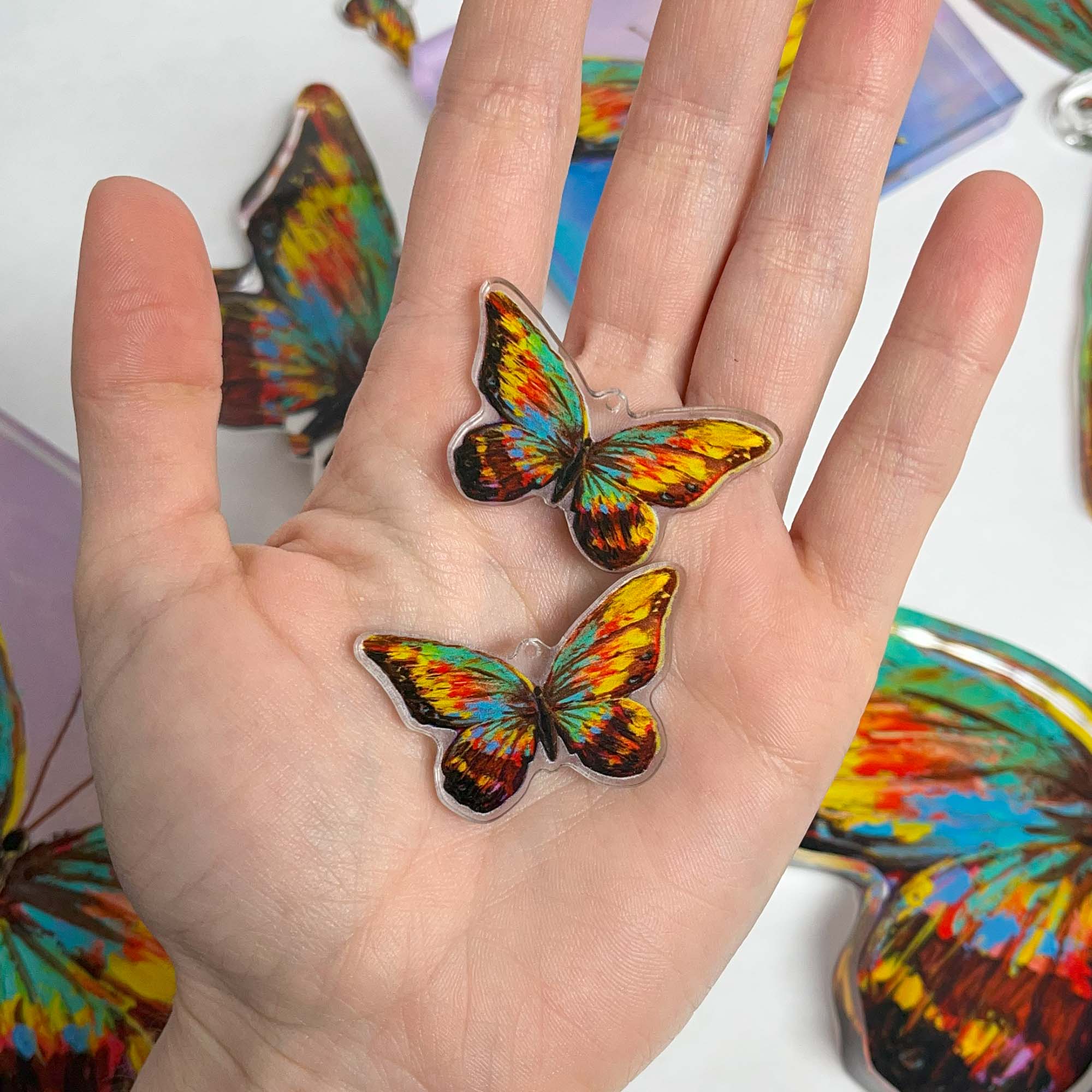 Hand holding acrylic cutout earrings featuring reproduced butterfly artwork.