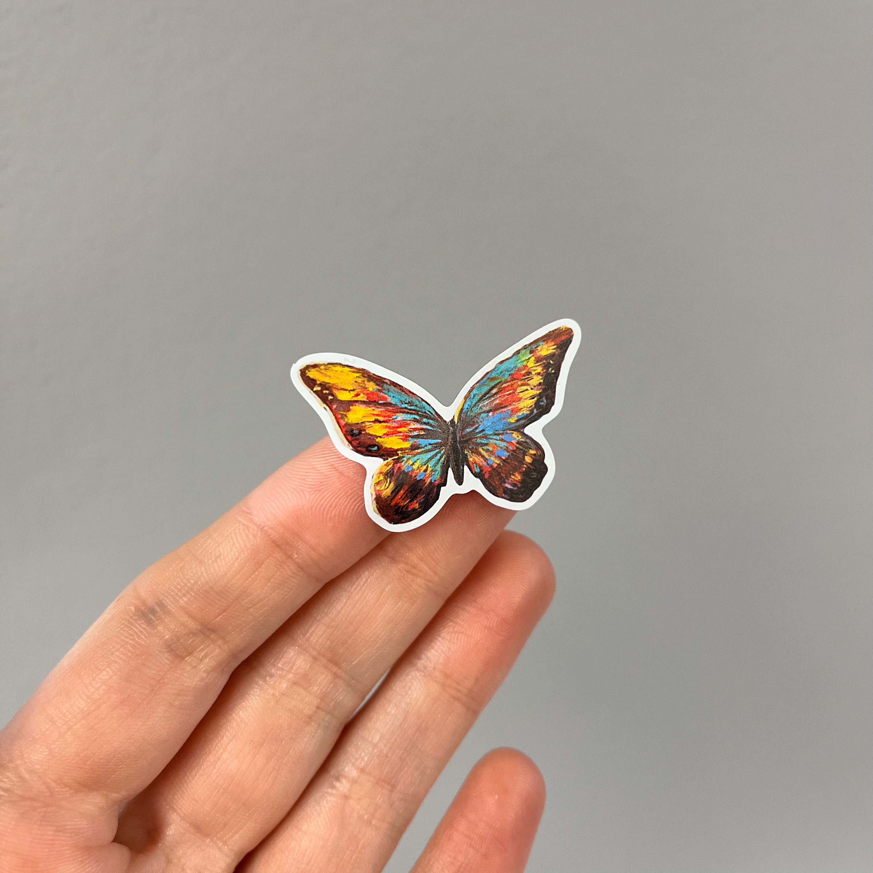 Hand holding a sticker featuring a print of a butterfly painting artwork.